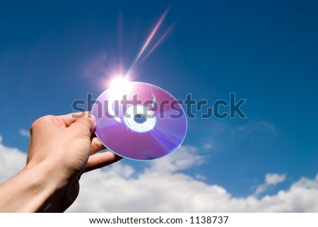 cd in hand, lens flare, blue sky and clouds as background