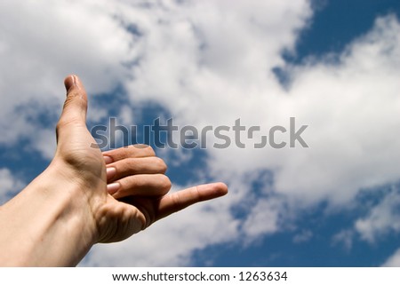 Hand showing a phone sign, blue sky with clouds as background
