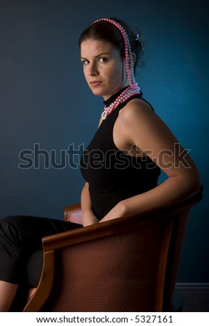 Gorgeous brunette in black with black pearls sitting in chair, classic shot