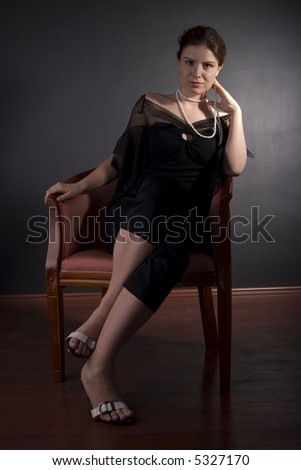 Gorgeous brunette in black with black pearls sitting in chair, classic shot, low key