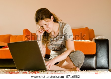 Young beautiful brunette women by the couch and surfing the internet on her laptop computer
