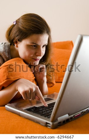 Young beautiful brunette women on the couch and surfing the internet on her laptop computer