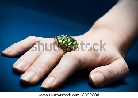 Big emerald ring on beautiful female hand, blue velvet as background