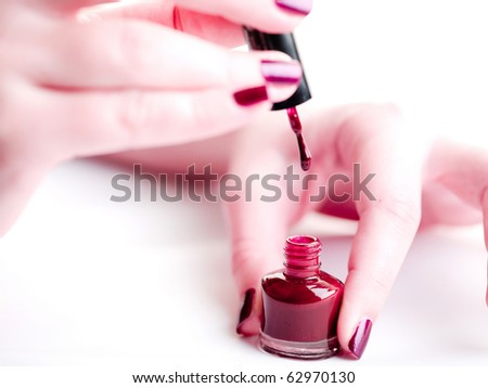 manicure process: High key shot of applying nail polish on nails, woman hand on white background and dark red nail polish