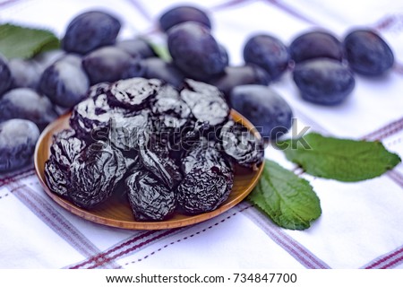 Dried prunes in a dish on a tablecloth on the background of fresh plums. Prunes and plums on the kitchen table closeup.