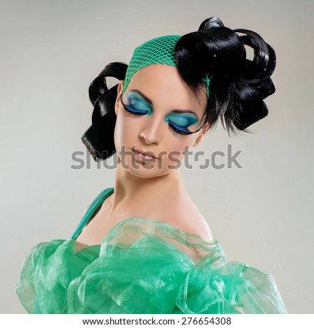 Portrait of beautiful young woman with long eyelashes, green colored eye lids black and styled hair.