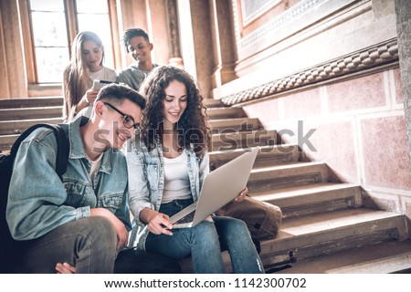 College life.Group of students using a laptop while sitting on stairs in university.