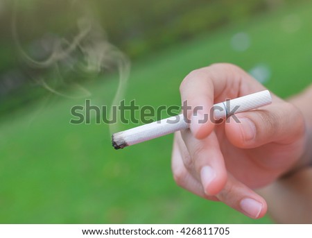 Selective focus Cigarette in the hand of a woman on the green grass background close up, World No tobacco day.