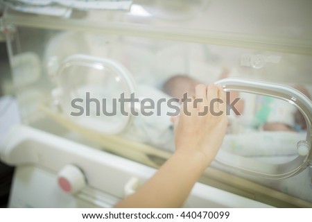 Selective focus Hand of a nurse or doctor checking a baby in the incubator , In neonatal intensive care unit of the hospital. Blurred background.