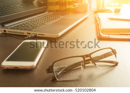 Selective focus  office table : eyeglass , mobile phone, laptop, note book and pencil on the wooden table. effect light added.