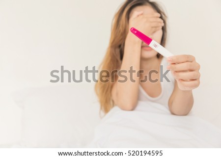 Selective focus Pregnancy test positive result smiling woman, young girl \
comfortless in bedroom, focus on hand. Blurred background.