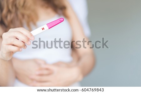 Selective focus happy couple hugging with positive pregnancy test in bedroom.