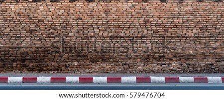 Old brown brick wall with concrete sidewalk and asphalt road with red and white traffic sign
