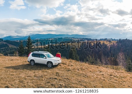 man in red coat near white suv car at hill with beautiful mountains view. road trip.