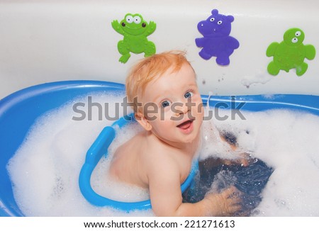 Baby boy with blue eyes in bath with toys plays with water