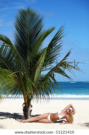 Young female in white bikini enjoying sunny day under palm tree on the tropical beach