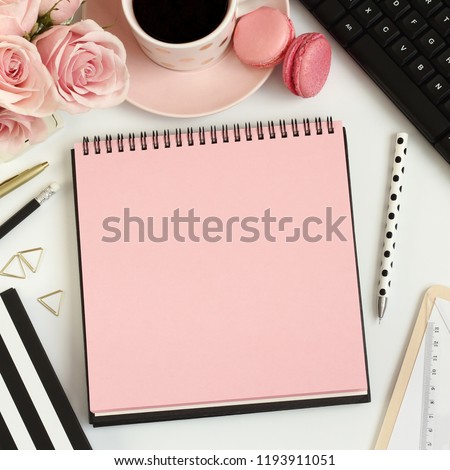 Office desk table with notebook, pink flowers, computer, cup of coffee and macarons. Coffee break, ideas, notes, goals, plan writing or sketching concept. Top view, flat lay.