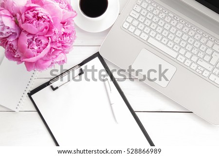 Office desk table with computer, supplies,  cup of coffee and peony flowers. White wooden background. Coffee break,  ideas, notes or plan writing concept. Top view, flat lay.