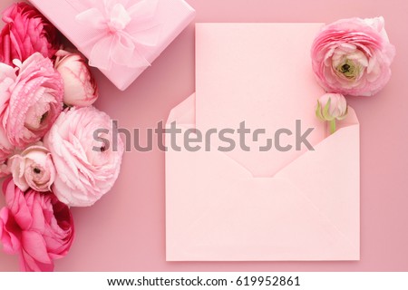 Pink ranunculus flowers, gift or present box and empty card with envelope on table. Mothers Day, Birthday, Valentines Day, Womens Day, celebration concept. Top view, flat lay.