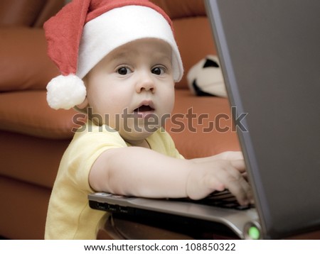 Baby boy in a hat of Santa writes on a laptop letter to Santa Claus