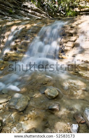 Water flowing the cascade on stones shined with sun beams