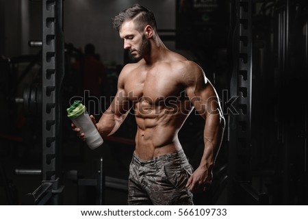 Handsome athletic fitness man holding a shaker and posing gym