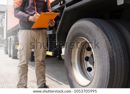Truck driver holding clipboard with writing for safety checks of tire truck.