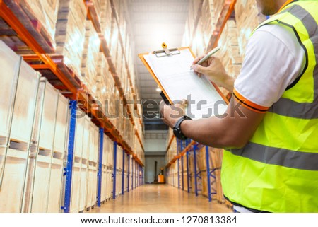 warehouse worker are holding a clipboard and writing on data sheet with inventory the products in large warehouse.