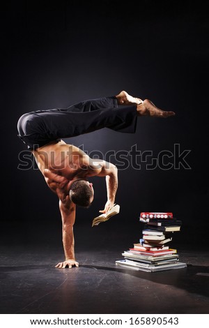 The strong man is standing on the one arm and reading book