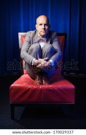 The bold man is sitting on the armchair