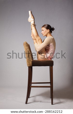 Beautiful young woman catch balance on chair in point shoes on gray background