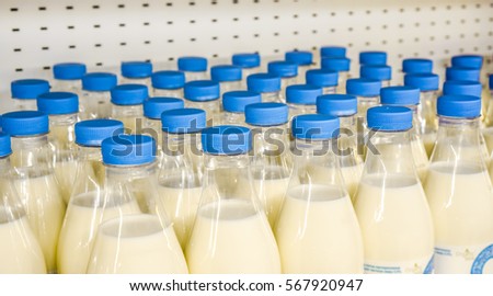 many plastic bottles with milk inside with bright blue covers against metal background in the shop, bottles with milk as dairy product for preparing breakfast wait for byers on market shelf