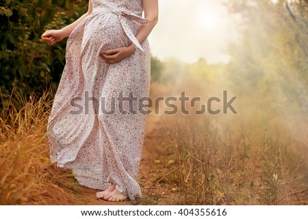 Stomach of the pregnant woman in a summer dress on the road outdoors