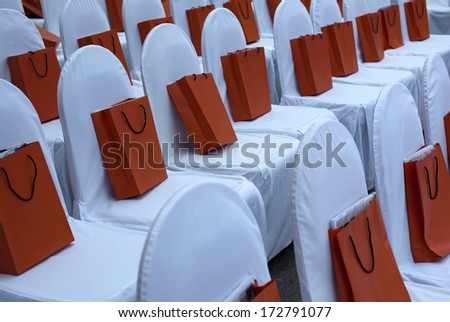 chairs in white covers in the hall for a fashion show gift bag on a white chair