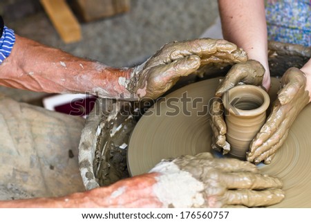 Old man teaching young woman how to work on pottery wheel