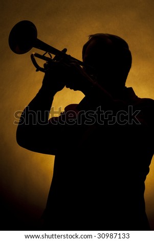 A silhouette of a trumpet being played by a trumpet player in the vertical format with copy space and a gold background.