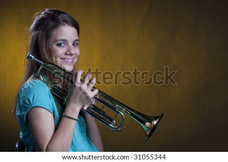 A teenage girl smiling and holding her trumpet music instrument isolated against a yellow spot light in the horizontal format with copy space.