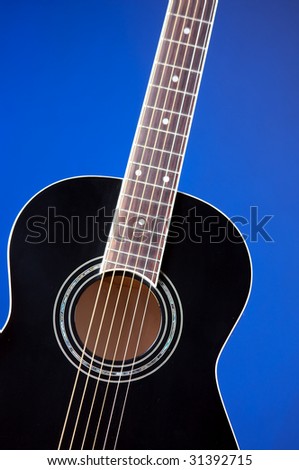 A black acoustic guitar isolated against a blue background in the vertical format with copy space.