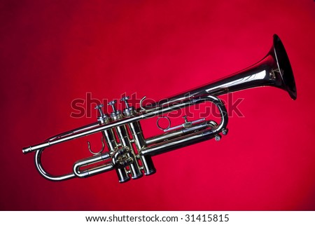 A gold colored brass trumpet isolated against a red background  in the horizontal format with copy space.