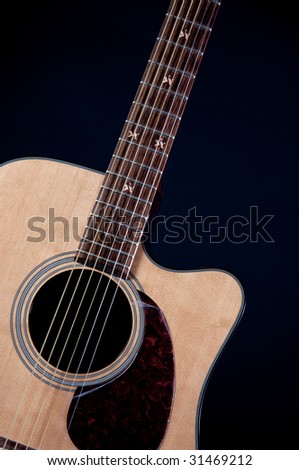 A natural finish acoustic guitar isolated against a black background in the vertical format with copy space.