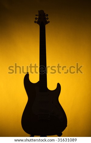 An electric guitar in silhouette against a gold or yellow background in the vertical format.