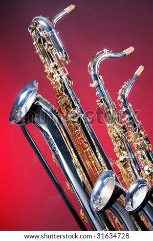 A set of three silver and gold saxophones including baritone, tenor, and alto against a red background in the vertical format.
