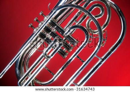 A silver marching French horn isolated on a red background in the horizontal format with copy space.