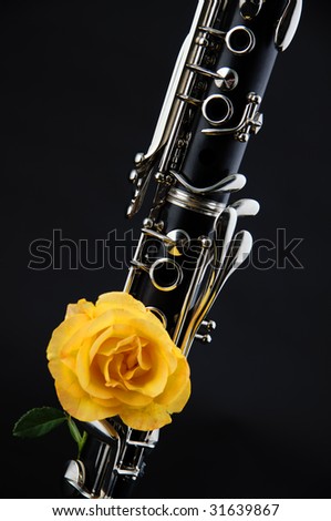 A soprano clarinet with a yellow rose against a black background in the vertical format with copy space.