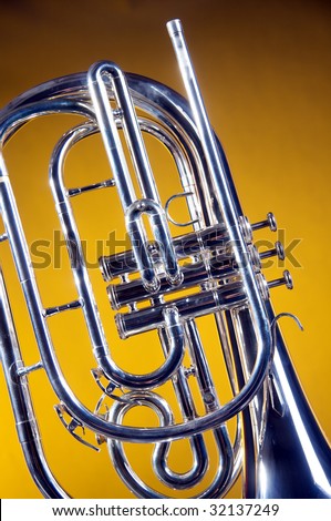 A silver marching French horn isolated on a yellow gold background in the vertical format with copy space.