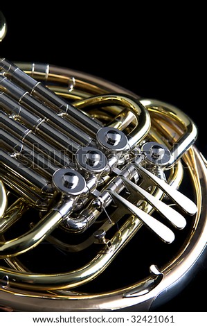 A brass and copper French horn isolated against a black background close up in the vertical format.