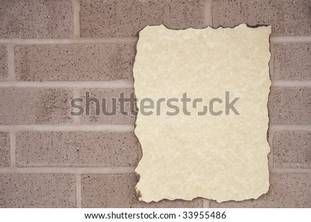 A piece of old paper burned on the edges against a brick wall in the horizontal format.