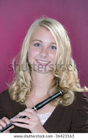 A blond blue eyed teenage female girl holding a wood piccolo flute against a pink background.