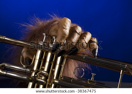 A Halloween gold brass trumpet in the clutches of a monster?s hand against a blue spotlight background  in the horizontal format.