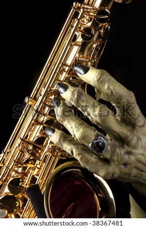 A Halloween holiday gold brass saxophone with a monster?s hand against a black background in the vertical format.